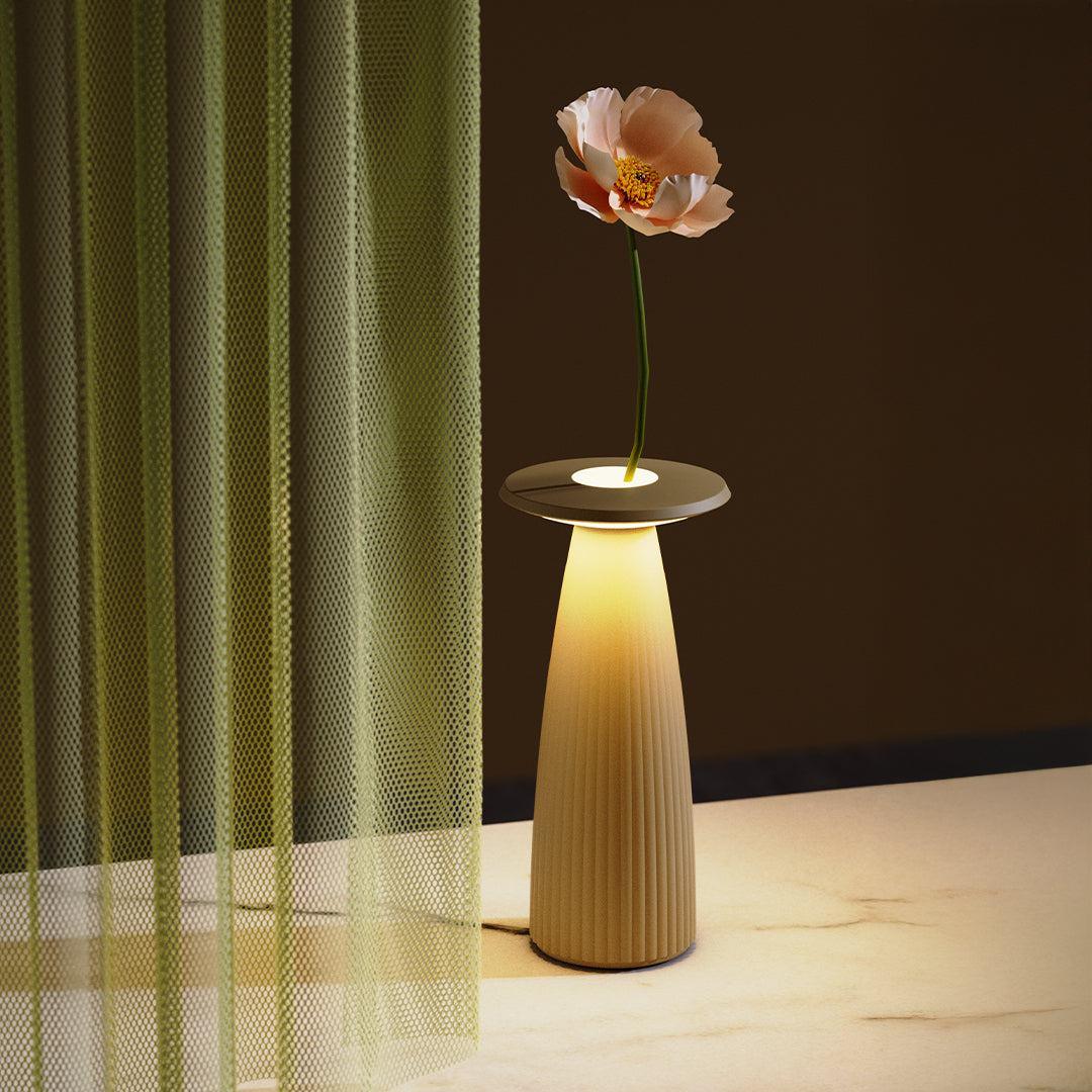 Flora cordless table lamp with LED light and flower vase design on marble surface near green curtain