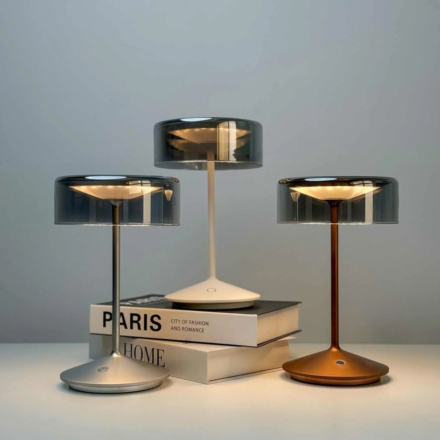 Three crystal cordless table lamps with smoky glass shades in silver, white, and bronze finishes on a light background