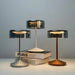 Three crystal cordless table lamps with smoky glass shades in silver, white, and bronze finishes on a light background