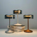 Three crystal cordless table lamps with smoky glass shades in silver, white, and bronze finishes on a light background