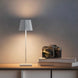 Plissé cordless table lamp with white pleated shade on wooden surface next to camera and books, modern LED rechargeable design