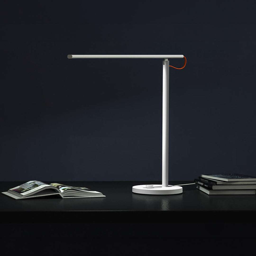 Mi LED Desk Lamp 1S modern white adjustable brightness desk lamp on black surface with books and dark background