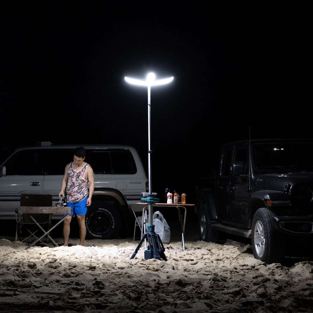 Portable petal tripod light illuminating outdoor camping area at night with man and vehicles nearby