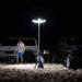 Portable petal tripod light illuminating outdoor camping area at night with man and vehicles nearby