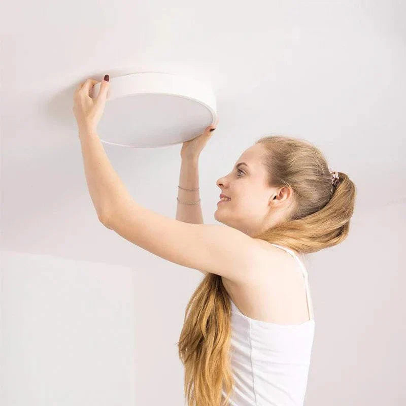 Woman installing round LED ceiling light with WiFi and Bluetooth connectivity in room