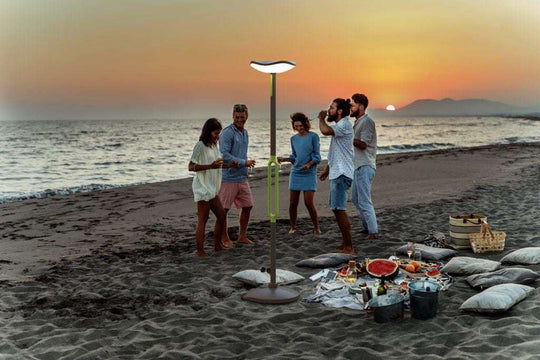 LUTEC Poppy solar LED floor lamp with Bluetooth speaker lighting a beach picnic at sunset
