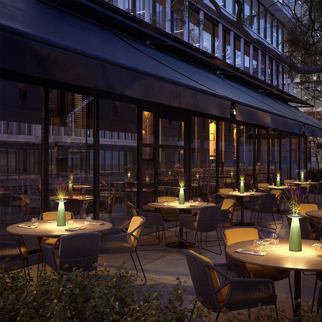 Outdoor dining area with several tables, each featuring a Flora cordless table lamp, combining ambient lighting and a flower vase.
