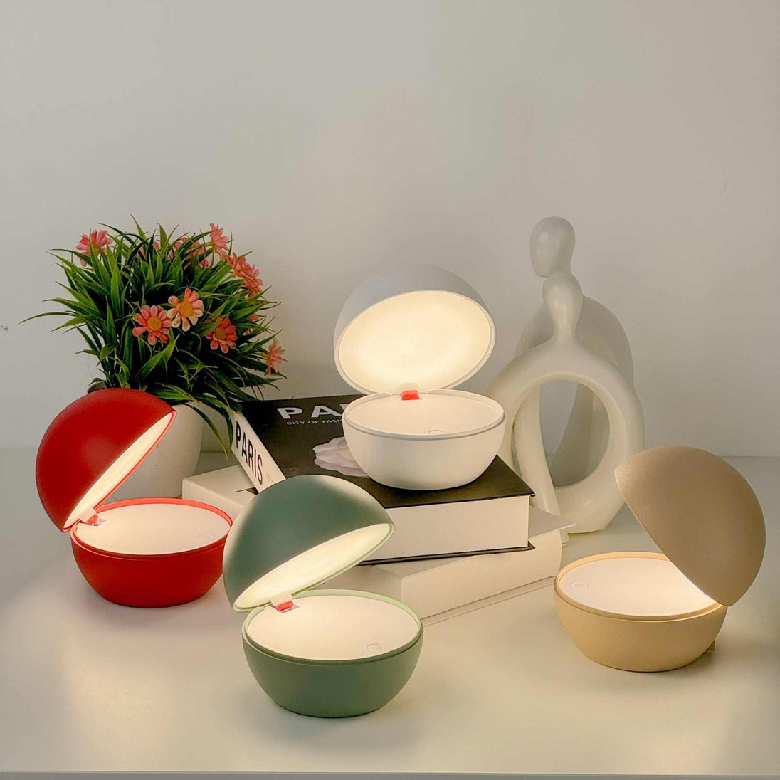 Goodnight cordless table lamps with round ball design in red, green, white, and beige emitting warm light on a bedside table with books and decor