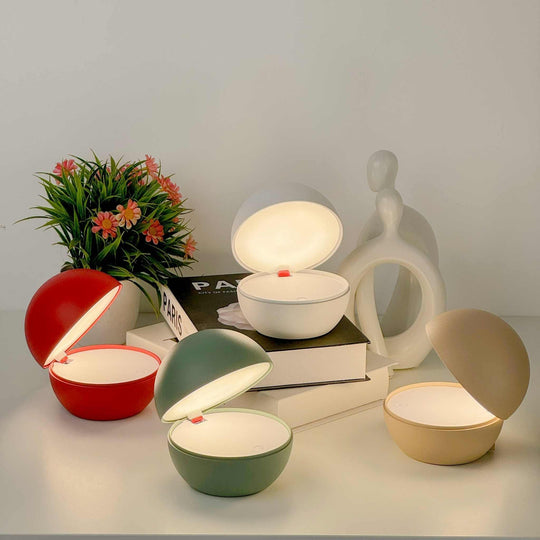 Goodnight cordless table lamps with round ball design in red, green, white, and beige emitting warm light on a bedside table with books and decor