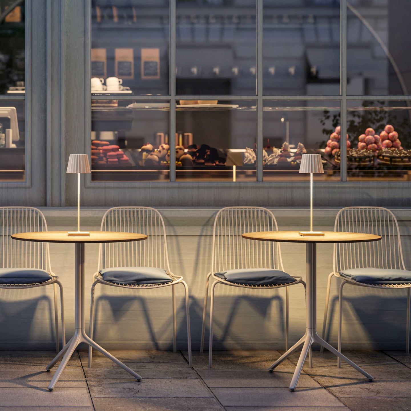 Cordless Plissé table lamps on cafe tables at night, showcasing modern design and ambient LED lighting.