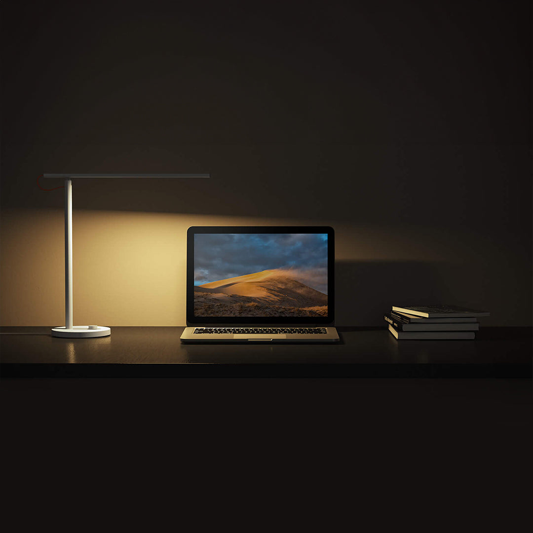 Mi LED Desk Lamp 1S illuminating a workspace with a laptop and books, showcasing its sleek design and brightness.