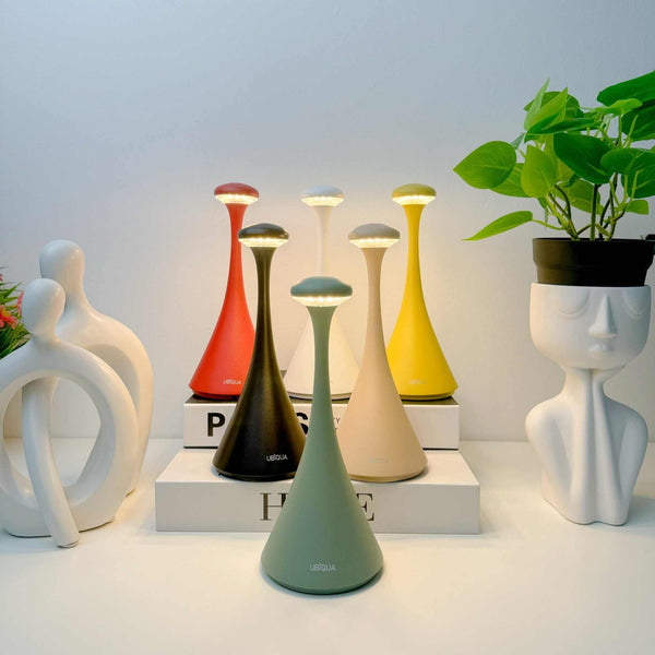 Pinup Maxi cordless rechargeable LED table lamps in various colors on a white surface with decorative sculptures and plants