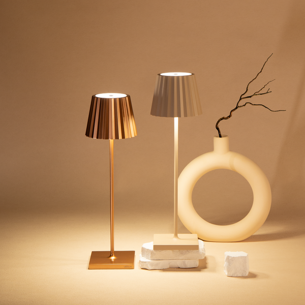 Plissé cordless table lamps with pleated shades, displayed on a beige surface next to a modern decorative vase.