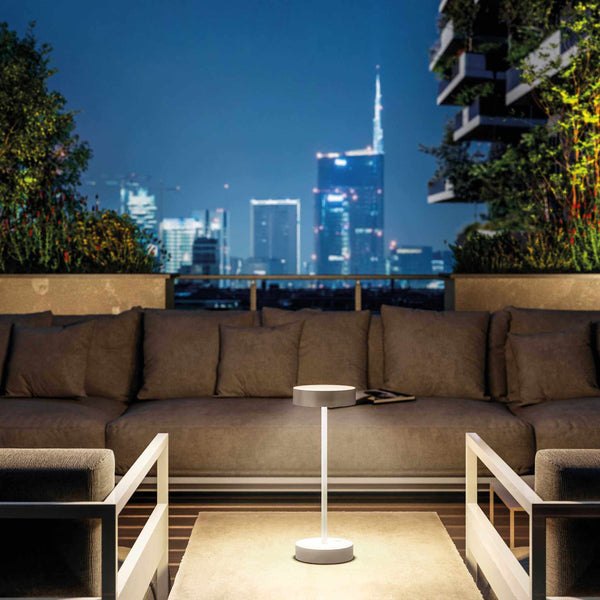 Minimalist portable LED lamp 'Standy Maxi' on outdoor table; sleek design, soft LED light, water and dust-resistant.