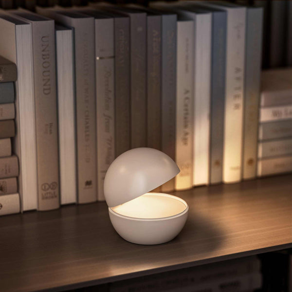 Cordless table lamp with round design on bookshelf, creating cozy ambiance.